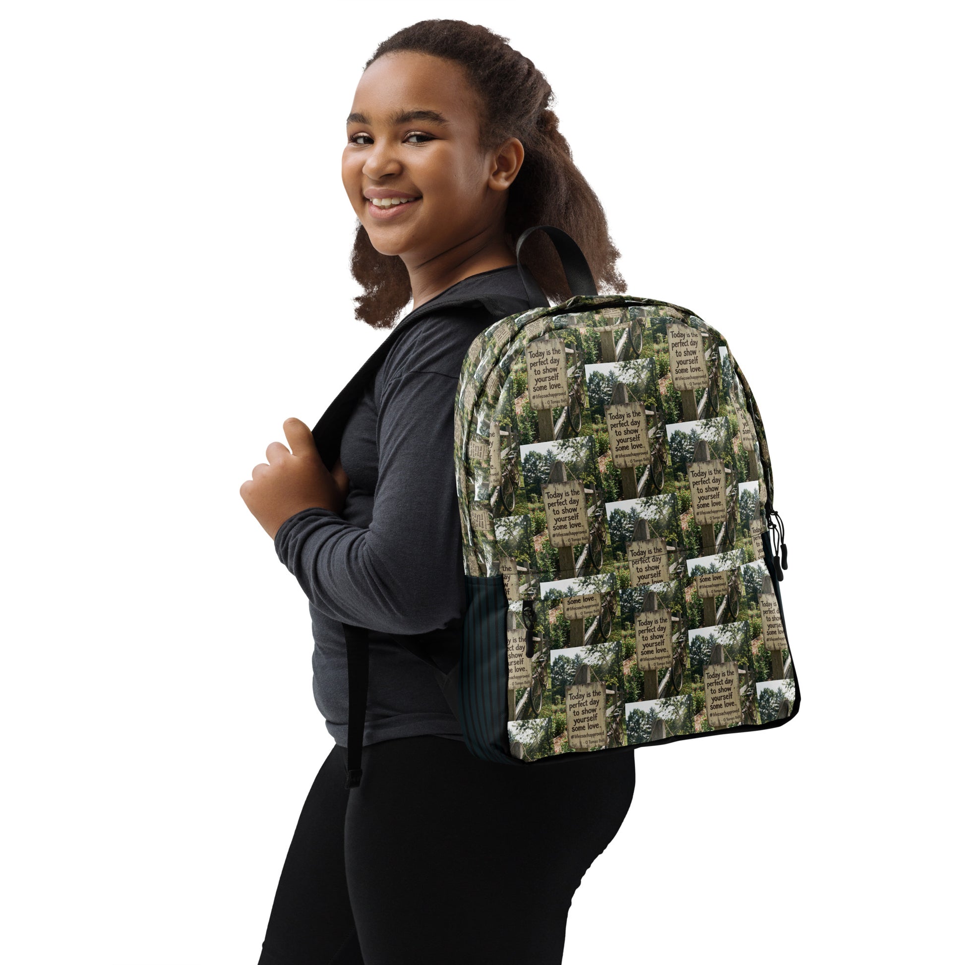 Self love backpack on person, green-and-beige collage print with black straps and accents