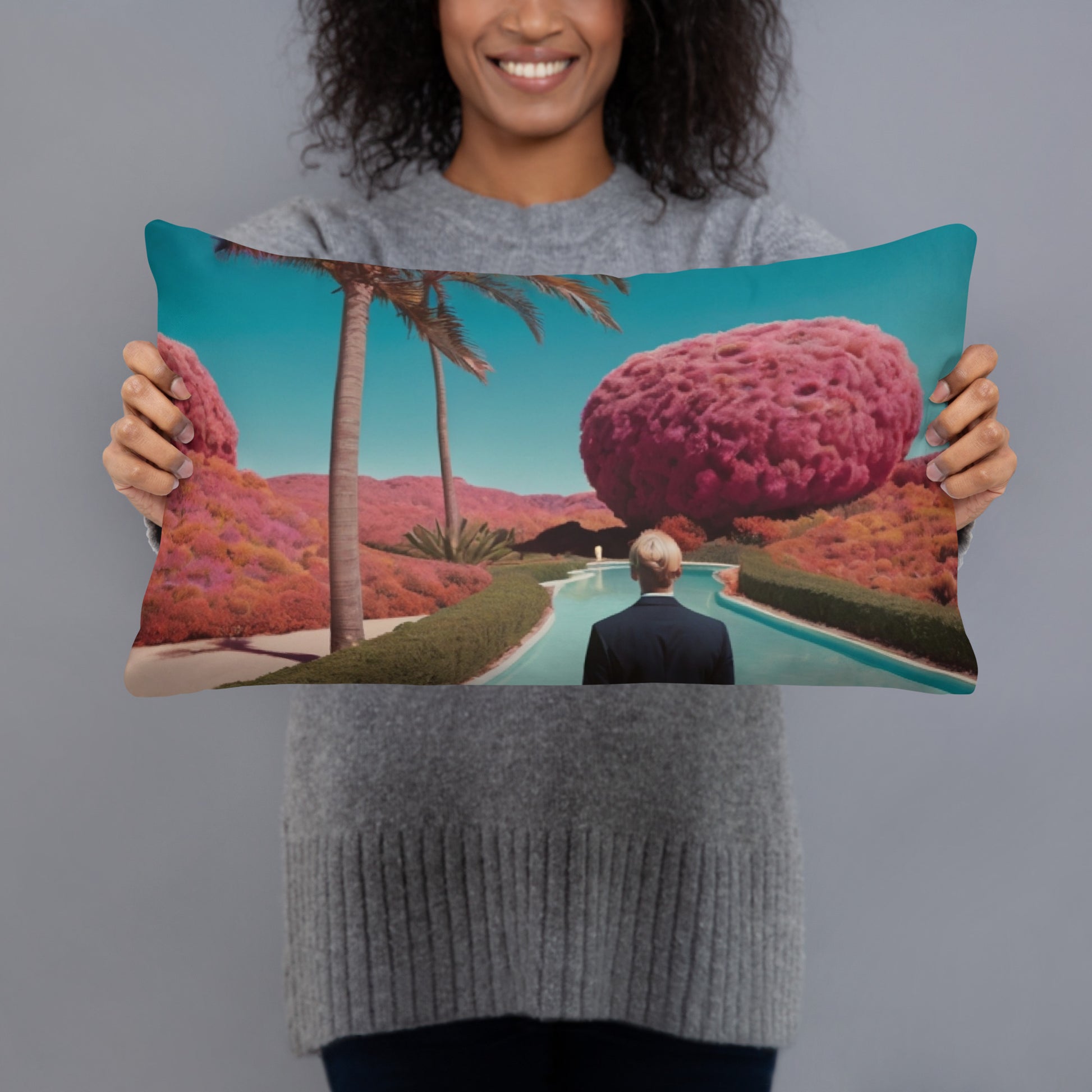 Square teal accent pillow held up, showing a palm-lined path with pink landscape