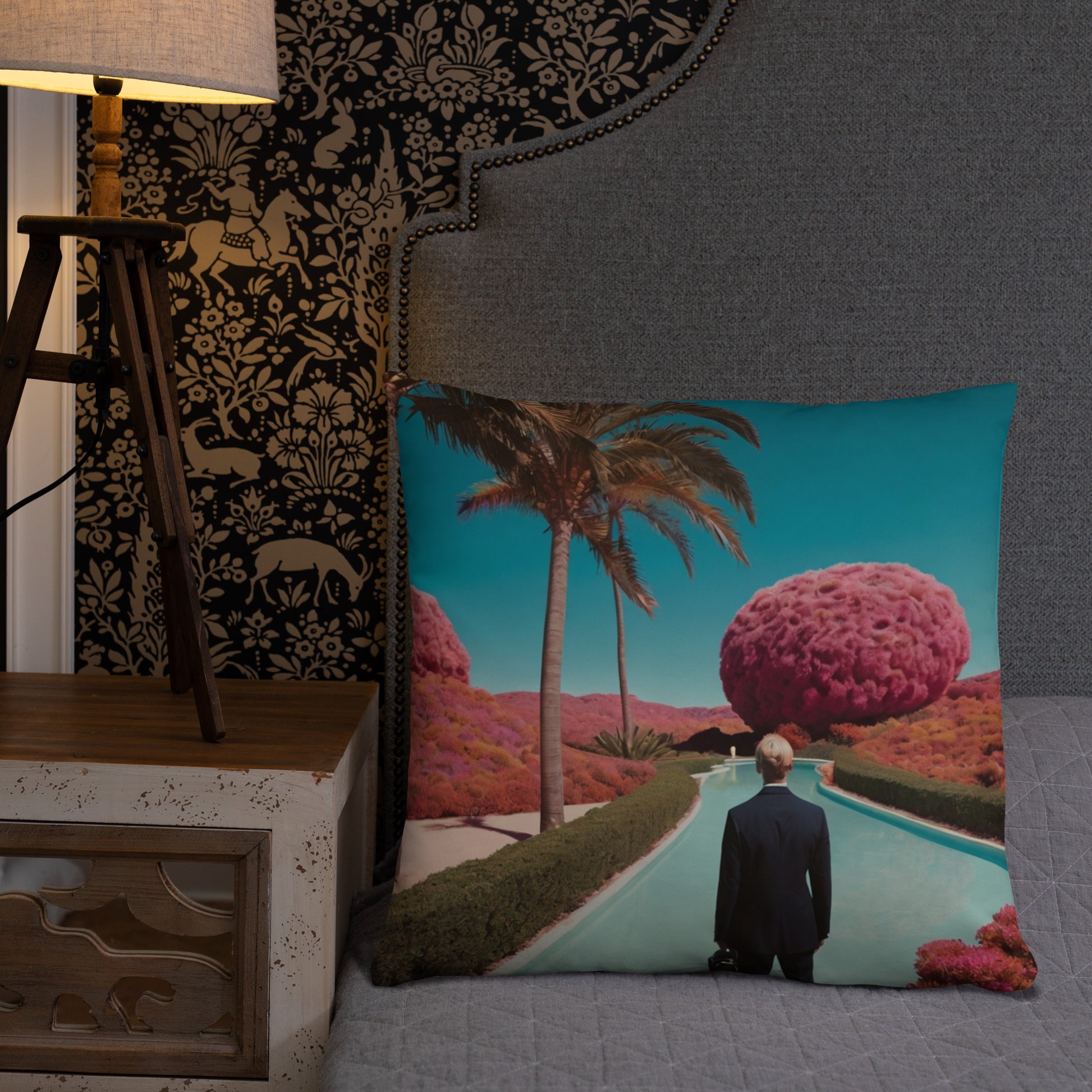 Teal accent pillow with a scenic pool, palm trees, and a man facing a large pink sphere