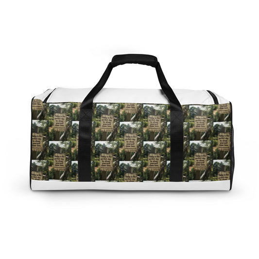 White duffle bag with black handles and repeating sign-and-landscape pattern
