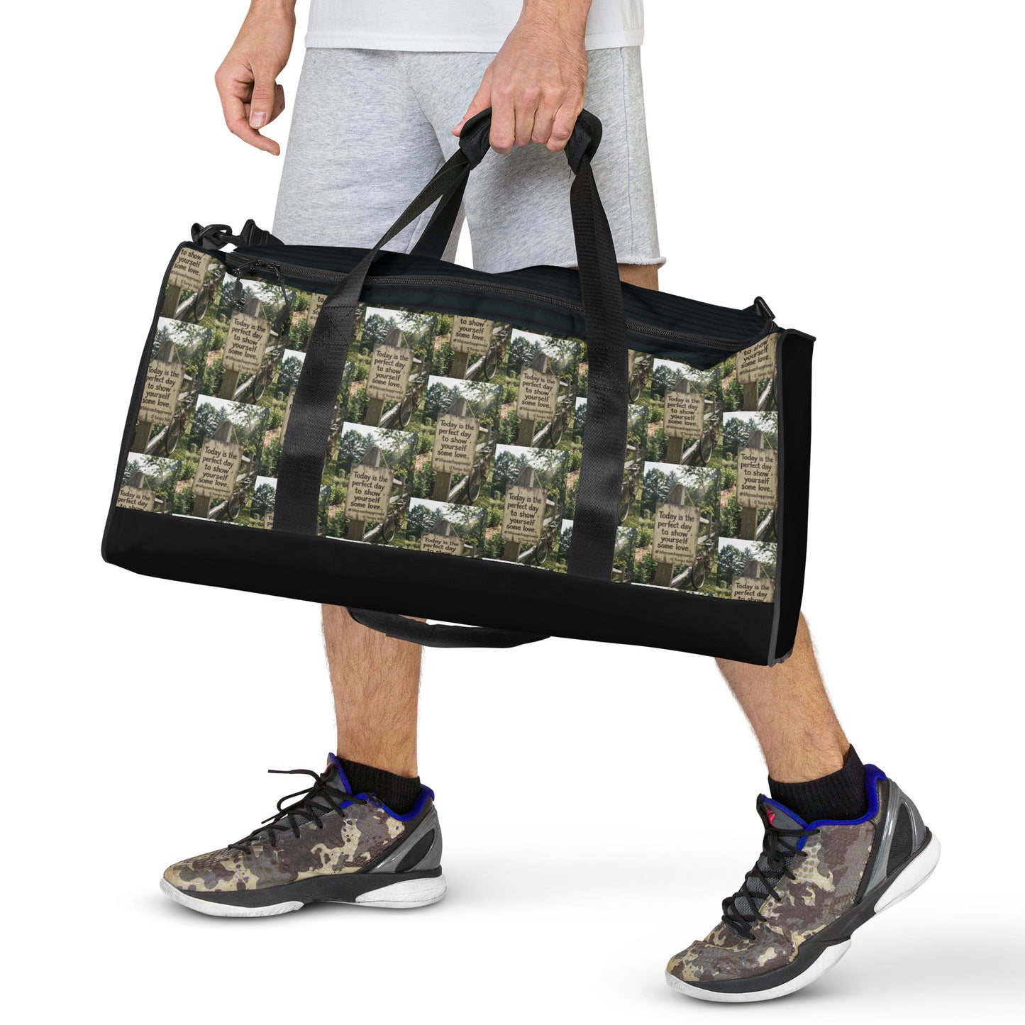 Black duffle bag with long handles and forest-and-quote graphic panel on the front.