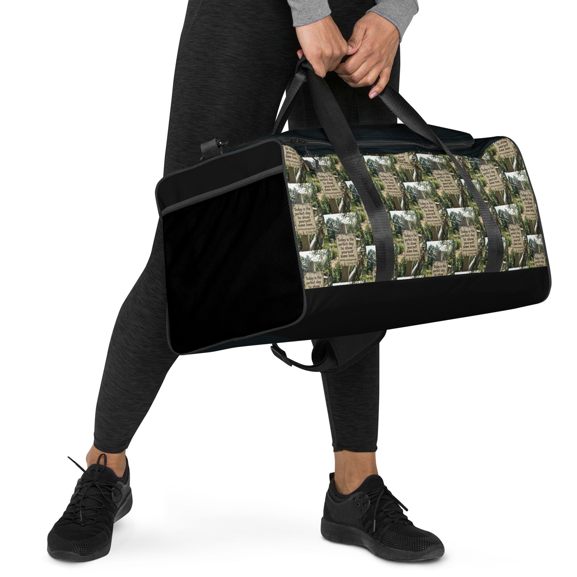 Black duffle bag with side pocket panel and forest-and-quote graphic exterior front.