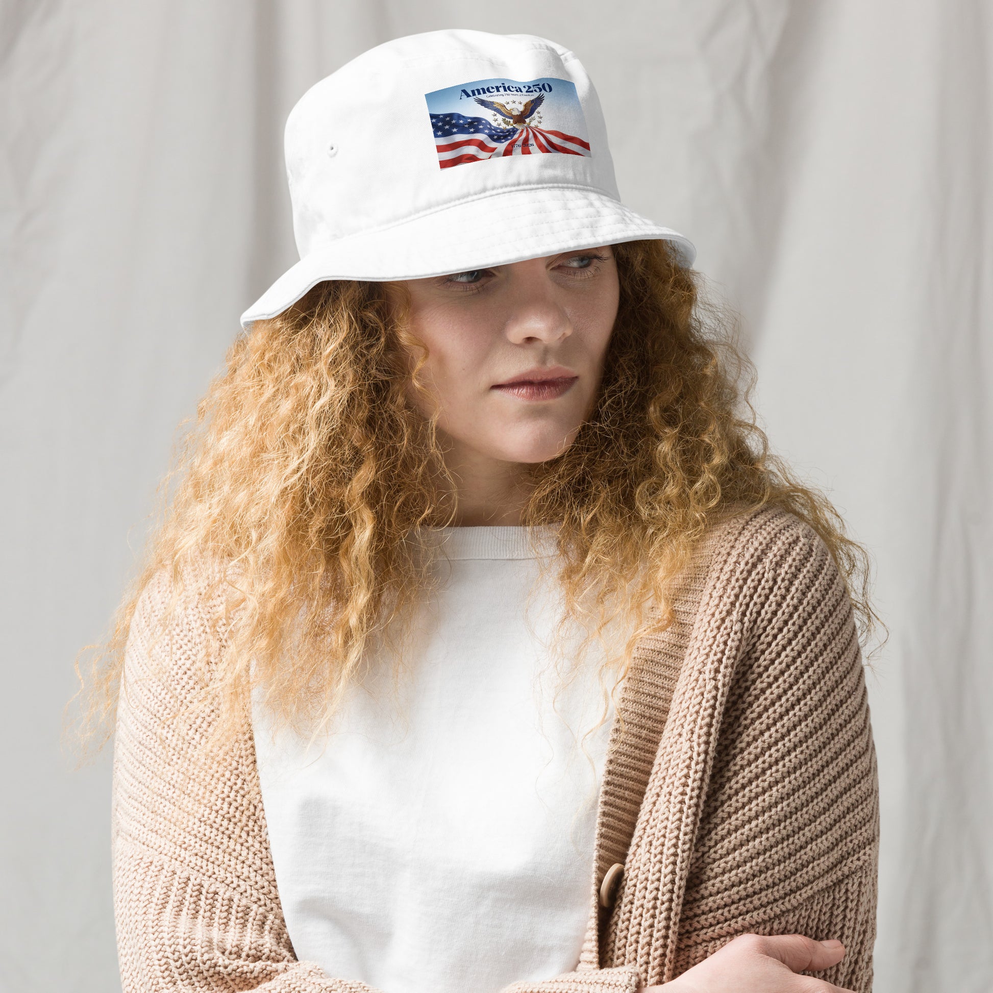 White bucket hat with front logo patch, worn with casual knit cardigan.