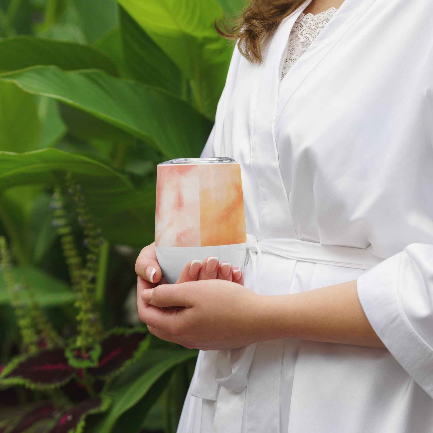 Wine tumbler with clear lid held in hands, white base, and orange-pink watercolor graphic.